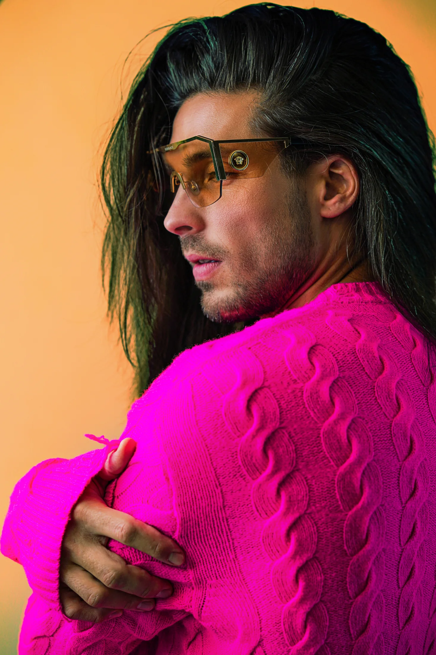 Alexander im pinken Stricklook mit selbstbewusstem Blick über die Schulter