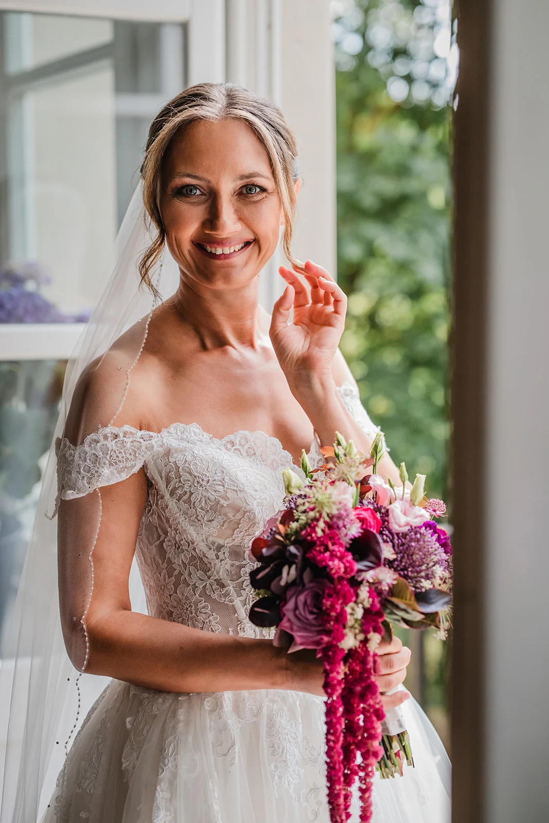 Natalie als Braut mit Blumenstrauß im hellen Fensterlicht